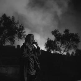 Eine Frau steht vor einem brennenden Hintergrund in der Nacht.