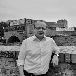 René Hobusch lehnt an der Moritzbastei. Er trägt ein weißes Hemd und eine graue Anzughose.