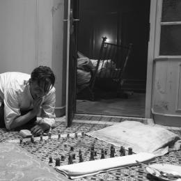 Protagonist Josef Bartok hockt auf dem Boden seines Badezimmers und spielt auf dem schwarz-weiß-gemusterten Fließen Schach.
