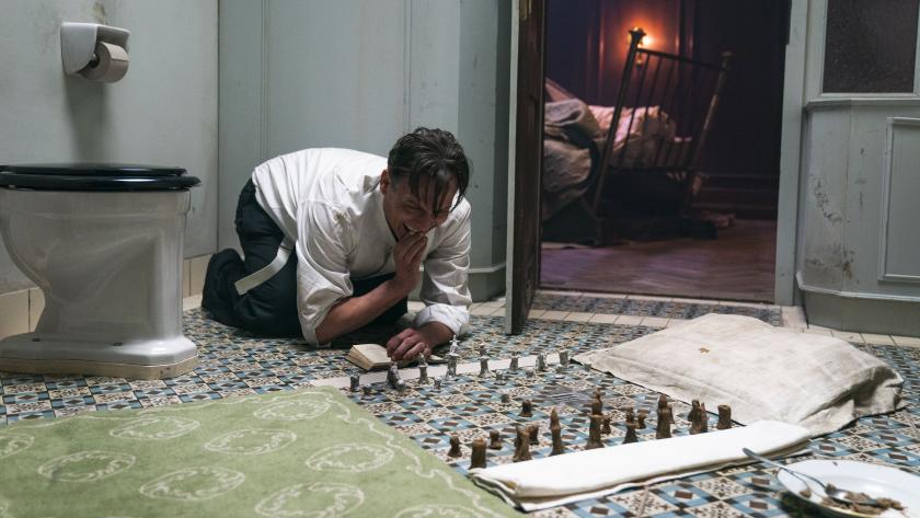 Protagonist Josef Bartok hockt auf dem Boden seines Badezimmers und spielt auf dem schwarz-weiß-gemusterten Fließen Schach.