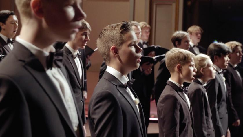 Mehrere Jungen stehen in Anzügen mit Fliegen nebeneinander und singen.