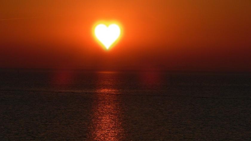Die Sonne geht in Herzform über dem Meer unter.